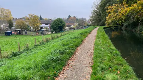 Tony Fisher/BBC A river with a path running alongside it which is on top of the bank leading down to a field and the back of Mr Hales's home.