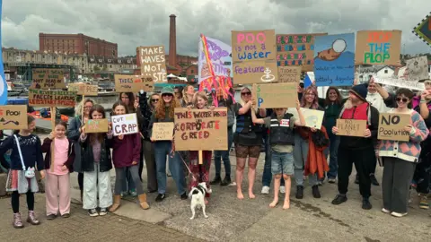 Dozens of people are holding placards against raw sewage looking at the camera