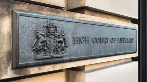 A sandstone wall with a grey plaque which reads "high court of justiciary"