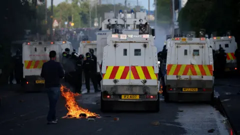 Police landrovers with fire behind them and police officers beside