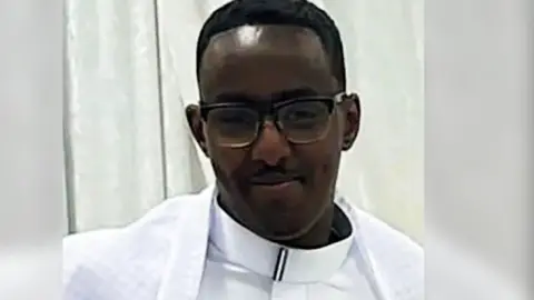 Mohamed Abdi Noor, a man with short dark hair and glasses, wearing white clothing and smiling.