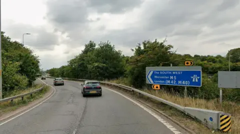 A motorway slip road on a cloudy and grey day. A blue sign reads The South West, Worcester M5, London M42, M40. 