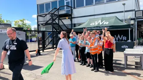A lady waving a flag and people cheering in the background as someone walks off the screen.