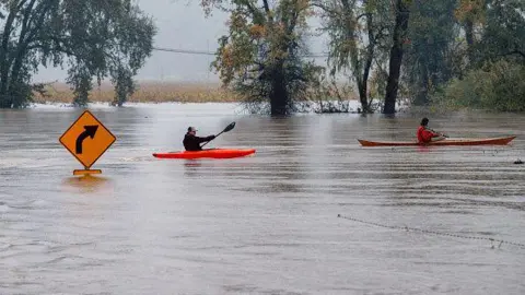 Kayakers row passed a street sign on a flooded road in California