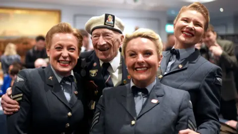 A veteran smiling and hugging three 'D-Day Darlings'