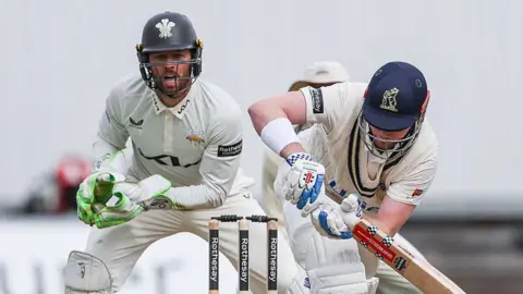 Left-handed Dan Mousley watchfully turns a ball to the legside as Surrey wicketkeeper Ben Foakes watches behind the stumps