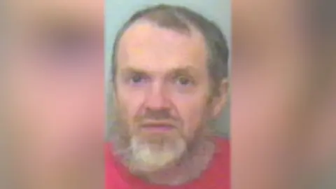 Suffolk Police Roy Barclay looks directly at the camera. He is wearing a red T-shirt and has a beard.