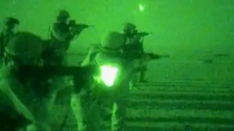 A night-vision image of troops firing their weapons in a desert landscape