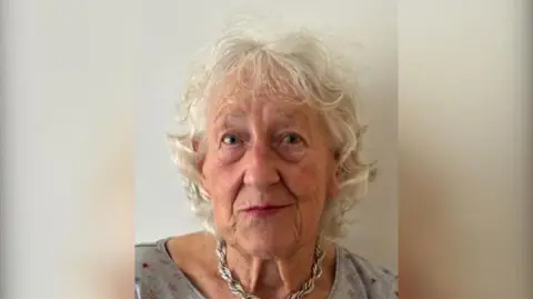 Margaret Worby: a grey-haired woman wearing a silver chain and a grey top looking ahead.