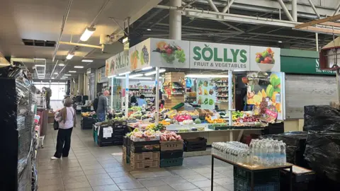 People shopping at Solly's Fruit and Vegetables store in a market