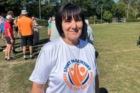 Annie Booth stands on a sports field wearing a white Sport Parkinson's T-shirt.