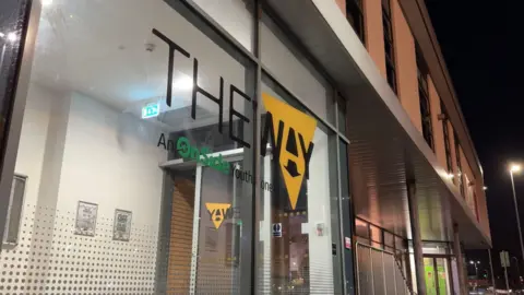 The Way Youth Zone in Wolverhampton. It is a large modern looking building with a glass frontage. It is night time. The Way logo is on the side. It is an OnSide Youth Zone. 