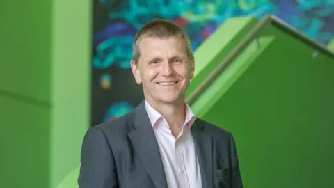 University of Sunderland Professor Scott Wilkes, who has greying hair and wears a grey suit jacket and pink shirt, smiling at the camera.