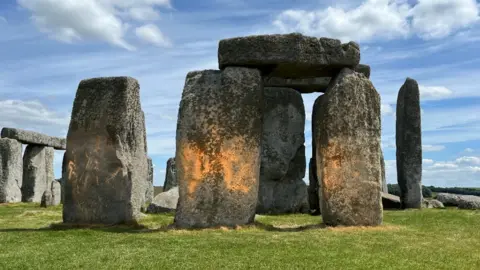 Three of the stones at Stonehenge are seen covered in splatters of orange powder paint. 