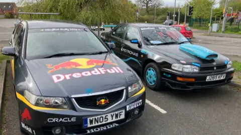 Two cars, viewed from the front. Both have branding on them, and the car to the right of the picture had a large teal coloured air intake on the bonnet
