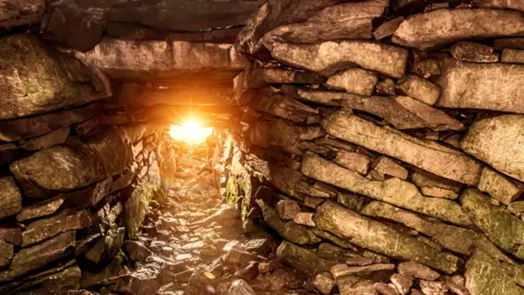 The sun shines through a gap in a wall of rocks of Slieve Gullion's passage tomb