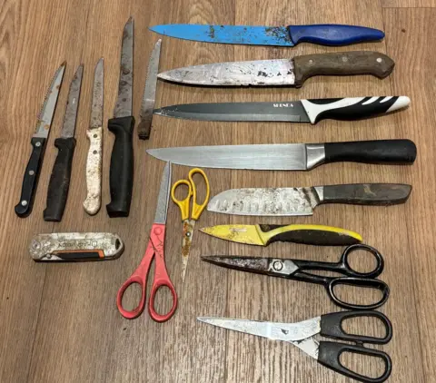 Clean Our Patch CIC A table displays 12 knives on it and four pairs of scissors. Some of them are rusty and dirty.