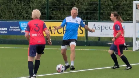 A man is about to kick of a football as two opposing players are closing into him.