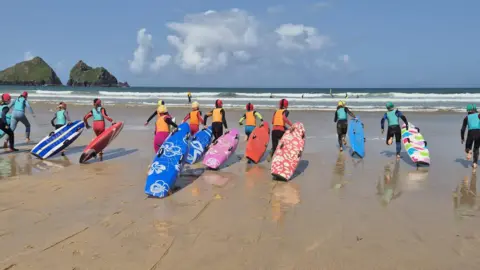 Young people with their surfboards heading into the sea