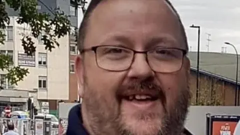 A smiling man with glasses stood on a high street