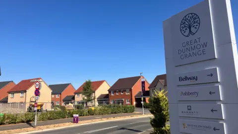 Henry Godfrey-Evans/BBC A wide shot of a sign saying Great Dunmow Grange with a number of developers listed and houses in the background
