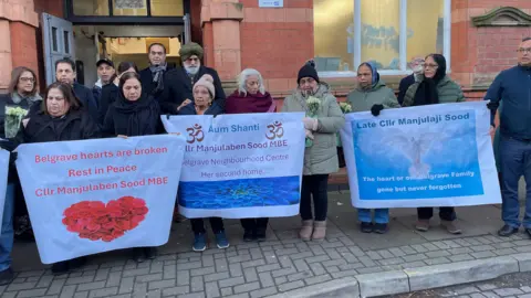 A group of people holding three banners which pay tribute to Manjula Sood