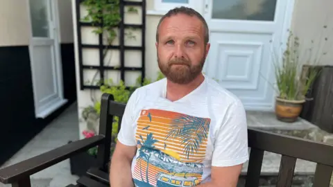 Man with short hair in t shirt sat on wooden bench