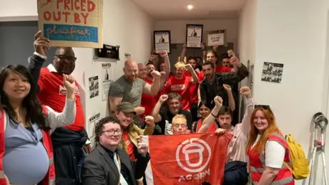 Residents many wearing red Acorn community union tops protest against rent increases with some holding a red Acorn flag and placards. 