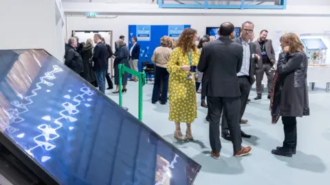 A large solar panel seen leaning on a stand, as people talk in groups in the background at the opening of the new green skills centre.