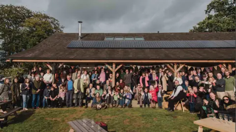 Blue Fox Photo A large group of people are waving at the camera, standing under a large barn with bunting slung under the balcony