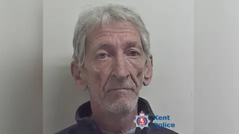 Mug shot of elderly man with grey hair and stubble. 