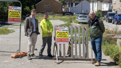 Residents stand beside anti-fly-tipping signs at the cleared Albert Road site near Sutton Station.