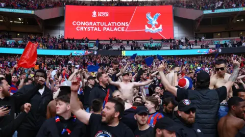 Reuters Crystal Palace fans celebrating in the stands at Wembley following the FA Cup semi final. Congratulations Crystal Palace is written on a red screen behind them