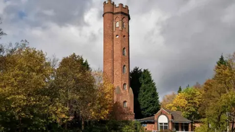 Birmingham Heritage Week a red brick tower surrounded by trees. The sky is grey and the tower has six arched windows