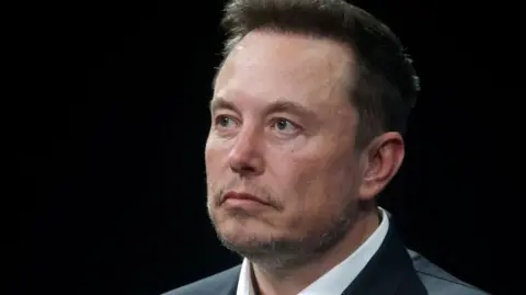 Getty Images A close up of Elon Musk's face. He has a serious expression and is looking away from the camera, against a black background.