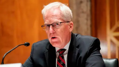 Getty Images Christopher Miller, who has short grey hair and glasses, and is wearing a black suit with a striped black-and-red tie, testifies at a Senate hearing in 2020