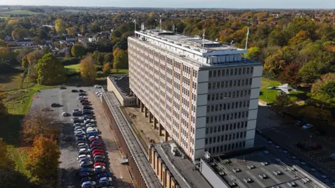 An aerial view of Norfolk County Council's County Hall which is a tall multi-storey building that has multiple windows. There are cars parked outside of the building on either side.
