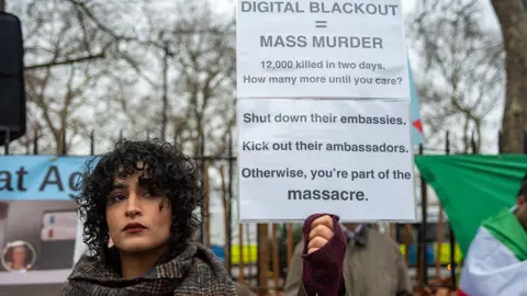 LightRocket via Getty Images a woman with curly hair holds up a sign that reads "digital blackout = mass murder"