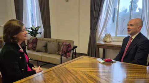 BBC Eluned Morgan is sat at a table and speaking to a man in a suit, Gareth Lewis.