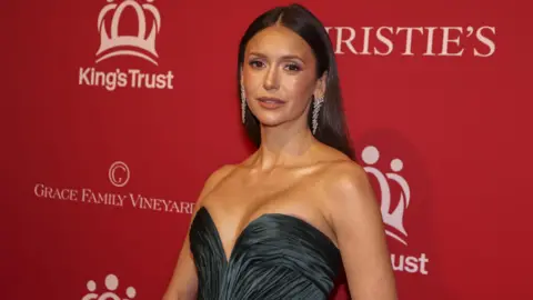 EPA/Shutterstock Nina Dobrev poses for picture in front of red King's Trust background