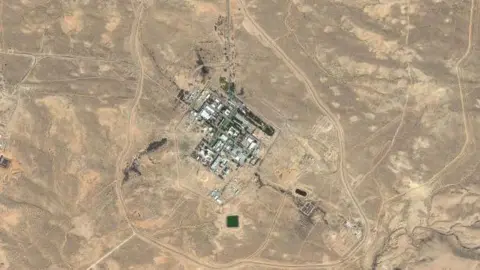 Maxar A satellite image shows a small grid of grey buildings in the desert.