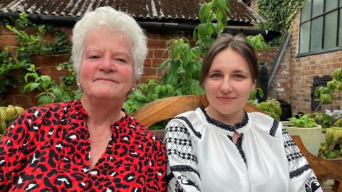Ukrainian refugee Katya and host Jill sit together outside