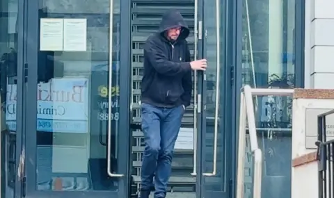 Craig Ware leaving Peterhead Sheriff Court in blue trousers and a dark hoodie pulled up.