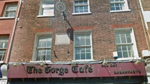 Google Cafe sign in red and black with row of bronze lights curved over two floors of the brick building with white windows stand above.