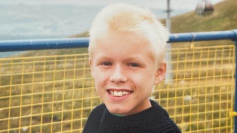A young boy with blond hair in front of a blue and yellow railing