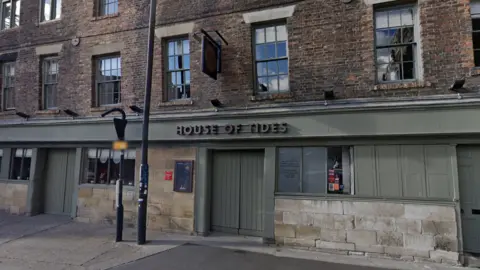 Google The exterior of the House of Tides restaurant. The bottom floor of the terraced, warehouse style building has wooden panels on it that are painted dark green. Some of the shutters on the windows are pulled to.