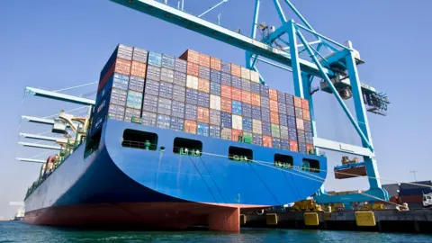 A ship with lots of container boxes on it being unloaded at a port