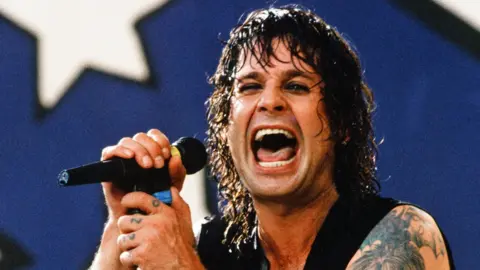 Ozzy Osbourne holding a microphone on stage, drenched in sweat and with a maniacal smile