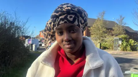 BBC A woman wearing a white coat and red hoodie looking at the camera.