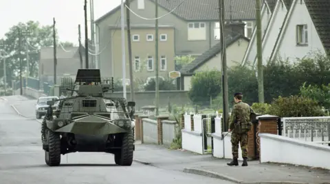 Getty Images A British soldier and a armoured saracen vehicle patrol on the streets. Houses are in the background.